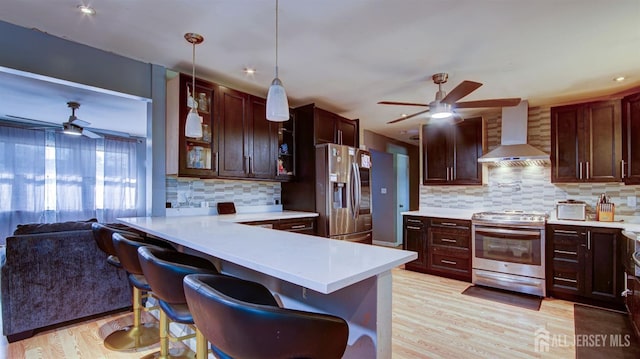 kitchen with kitchen peninsula, wall chimney exhaust hood, a breakfast bar, stainless steel appliances, and decorative light fixtures