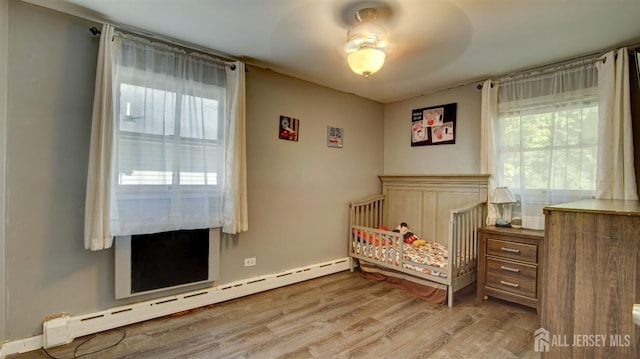 bedroom featuring a nursery area, ceiling fan, light hardwood / wood-style floors, and a baseboard radiator