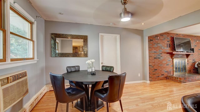 dining area with a brick fireplace, a wall mounted AC, baseboard heating, ceiling fan, and light hardwood / wood-style floors