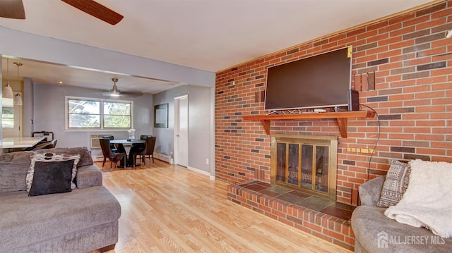 living room featuring a wall mounted air conditioner, a brick fireplace, ceiling fan, hardwood / wood-style flooring, and a baseboard radiator