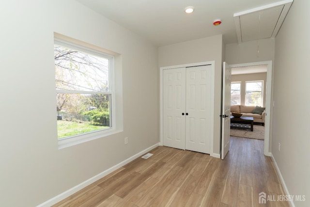 unfurnished bedroom with visible vents, a closet, baseboards, attic access, and light wood-type flooring