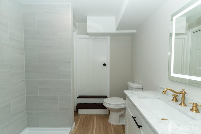 bathroom featuring wood finished floors, a tile shower, toilet, and vanity