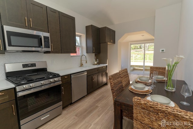 kitchen with decorative backsplash, a sink, light wood-style floors, stainless steel appliances, and light countertops