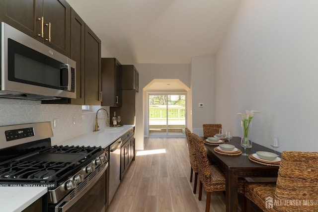 kitchen featuring a sink, light wood-style flooring, light countertops, arched walkways, and appliances with stainless steel finishes
