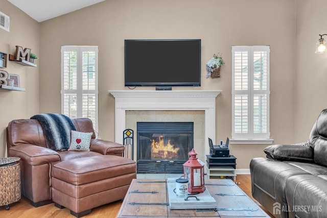 living area featuring light wood-type flooring, lofted ceiling, and a tile fireplace