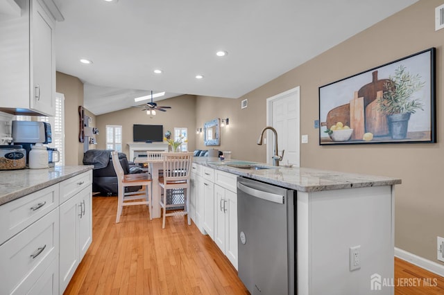 kitchen featuring stainless steel dishwasher, a sink, ceiling fan, light wood-style flooring, and open floor plan