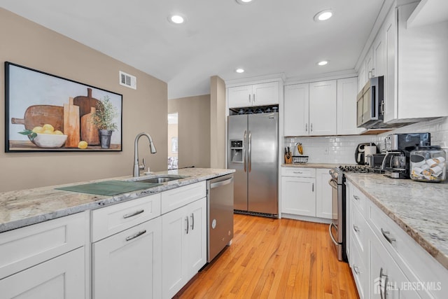 kitchen featuring stainless steel appliances, white cabinetry, light wood-type flooring, a sink, and recessed lighting