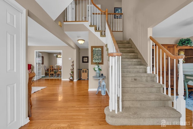 stairway featuring wood finished floors, baseboards, and a high ceiling