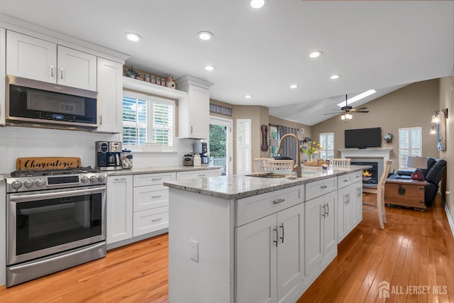 kitchen featuring stainless steel appliances, a sink, a lit fireplace, ceiling fan, and open floor plan