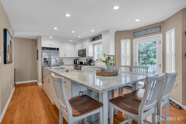 kitchen with appliances with stainless steel finishes, baseboards, white cabinets, healthy amount of natural light, and recessed lighting