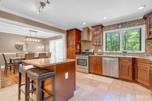 kitchen featuring stainless steel appliances, wall chimney exhaust hood, decorative backsplash, brown cabinetry, and crown molding