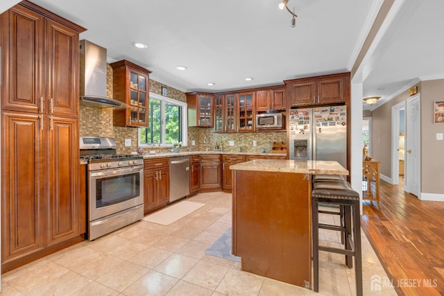 kitchen featuring wall chimney exhaust hood, stainless steel appliances, ornamental molding, decorative backsplash, and light stone counters
