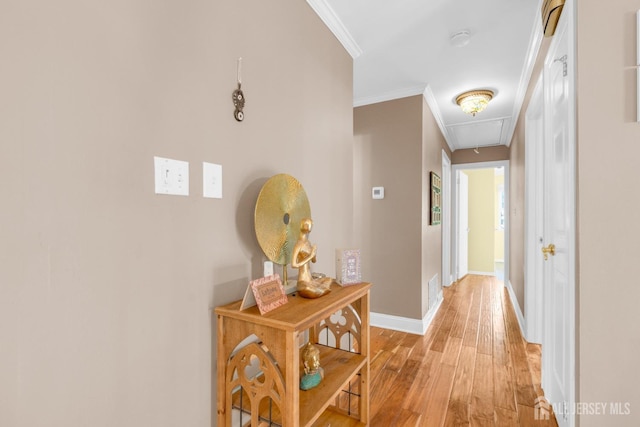 corridor with attic access, light wood-style floors, ornamental molding, and baseboards