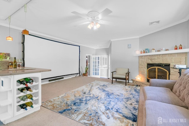 living room featuring carpet flooring, ornamental molding, ceiling fan, and a stone fireplace