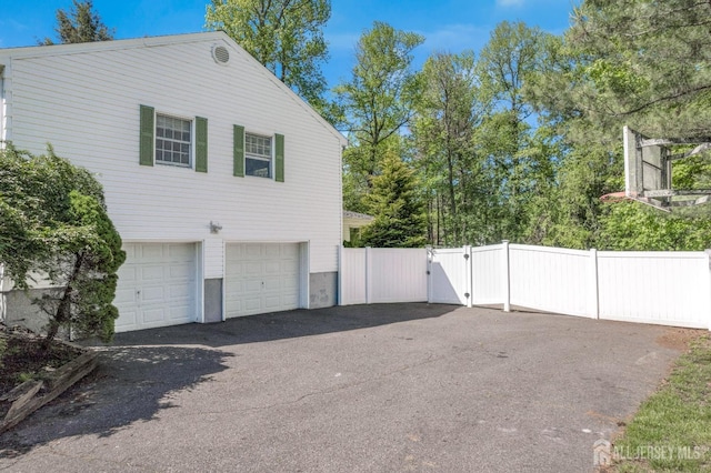 view of property exterior with a gate, an attached garage, fence, and asphalt driveway