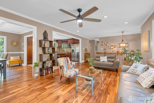 living room featuring light wood-style flooring, a ceiling fan, recessed lighting, baseboards, and ornamental molding