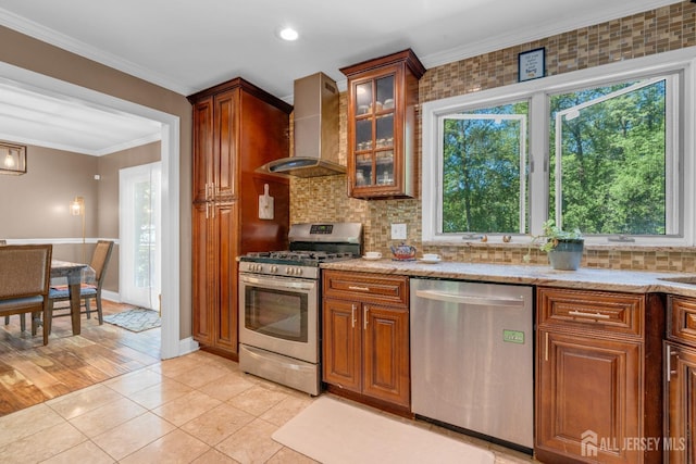 kitchen with appliances with stainless steel finishes, wall chimney exhaust hood, healthy amount of natural light, brown cabinets, and crown molding