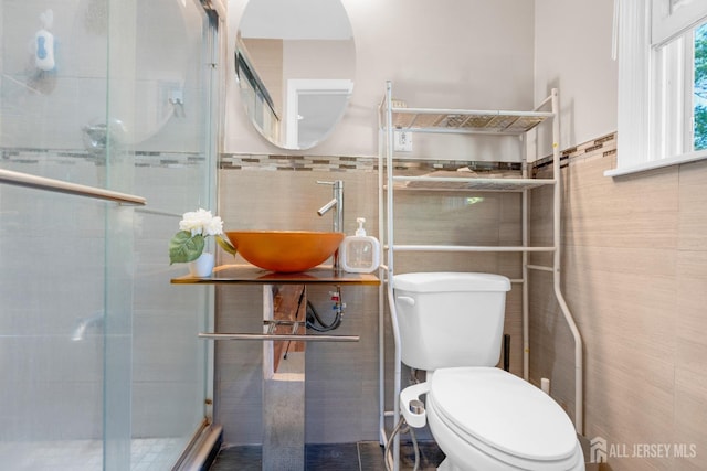 bathroom featuring tile walls, toilet, a sink, a shower stall, and a wainscoted wall