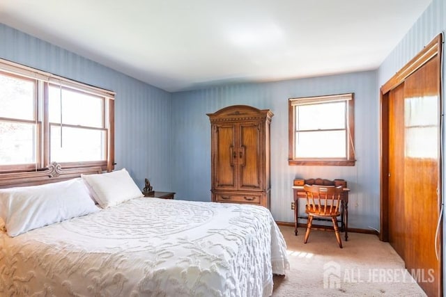 bedroom with multiple windows, light carpet, a closet, and baseboards