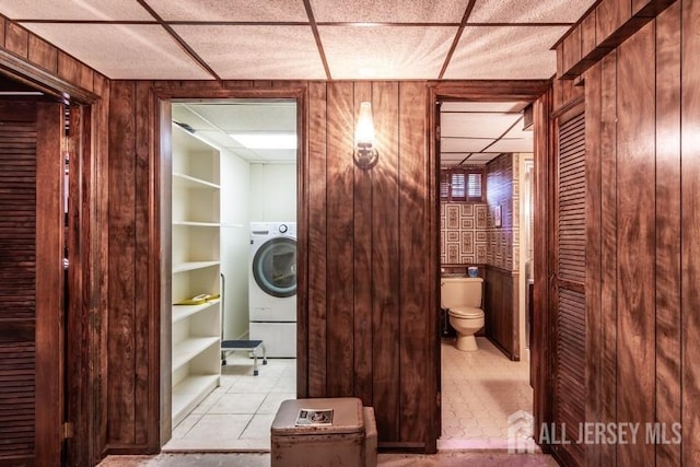 bathroom with a paneled ceiling, washer / clothes dryer, wooden walls, toilet, and tile patterned flooring