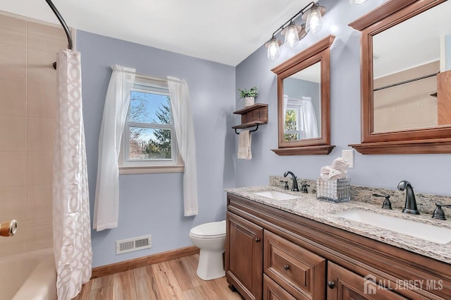 bathroom with wood finished floors, toilet, baseboards, double vanity, and shower / tub combo