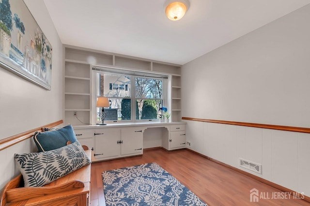 office area with light wood-style floors, built in study area, built in shelves, and a wainscoted wall