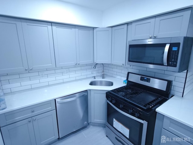 kitchen featuring tasteful backsplash, gray cabinets, light countertops, appliances with stainless steel finishes, and a sink