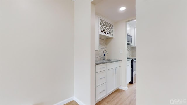 kitchen with appliances with stainless steel finishes, tasteful backsplash, light stone counters, light hardwood / wood-style floors, and white cabinets