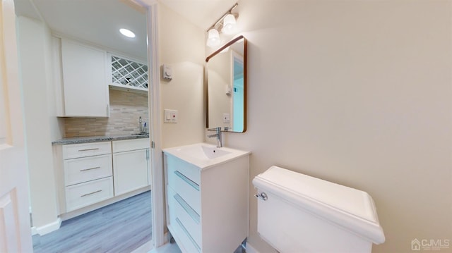 bathroom featuring vanity, hardwood / wood-style floors, decorative backsplash, and toilet