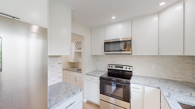 kitchen with light stone counters, stainless steel appliances, backsplash, and white cabinets