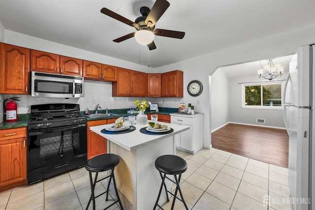 kitchen with white fridge, a breakfast bar, light tile patterned floors, and black range with gas cooktop