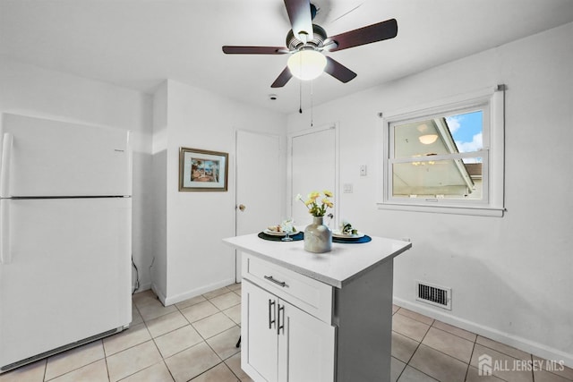 kitchen with light tile patterned flooring, a center island, white fridge, ceiling fan, and white cabinets