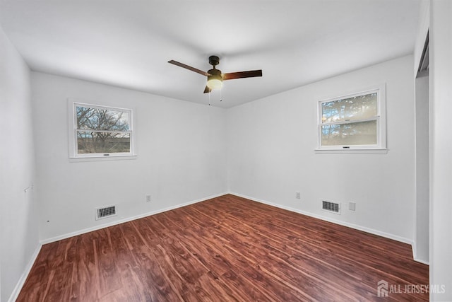 empty room featuring ceiling fan, a healthy amount of sunlight, and dark hardwood / wood-style flooring