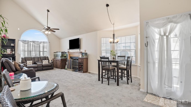 carpeted living area featuring a fireplace, high vaulted ceiling, a wealth of natural light, and ceiling fan with notable chandelier