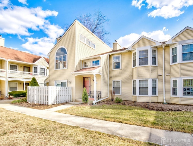 townhome / multi-family property featuring a front yard, fence, and a chimney