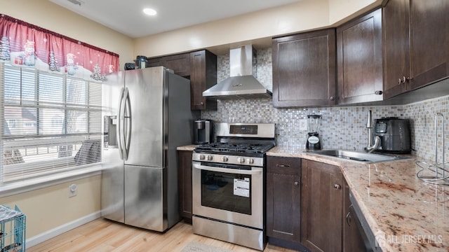 kitchen with dark brown cabinetry, wall chimney range hood, stainless steel appliances, and decorative backsplash