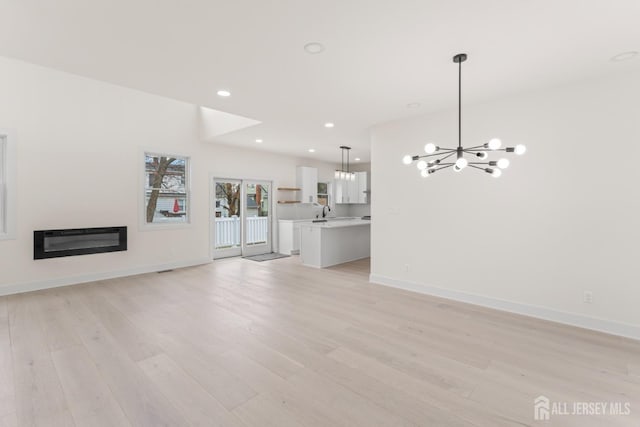 23 Redwood Ave, Edison, NJ 08817 - unfurnished living room with a chandelier, light wood-type flooring, recessed lighting, baseboards, and a glass covered fireplace