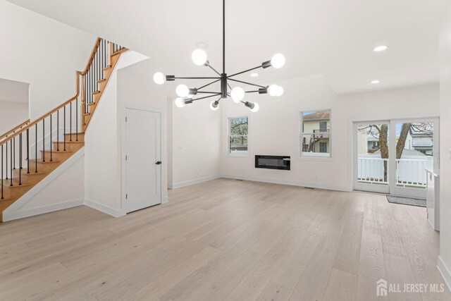 unfurnished living room with stairs, a healthy amount of sunlight, a chandelier, and light wood finished floors