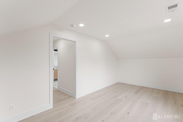 additional living space with light wood finished floors, vaulted ceiling, and visible vents