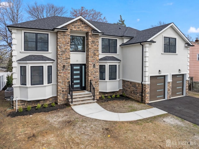 traditional-style home featuring stone siding, an attached garage, a shingled roof, stucco siding, and aphalt driveway