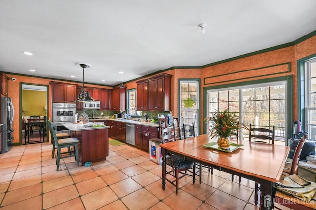 kitchen with light tile patterned floors, appliances with stainless steel finishes, hanging light fixtures, a kitchen island, and decorative backsplash