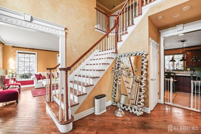 stairs featuring crown molding, wood-type flooring, and a high ceiling