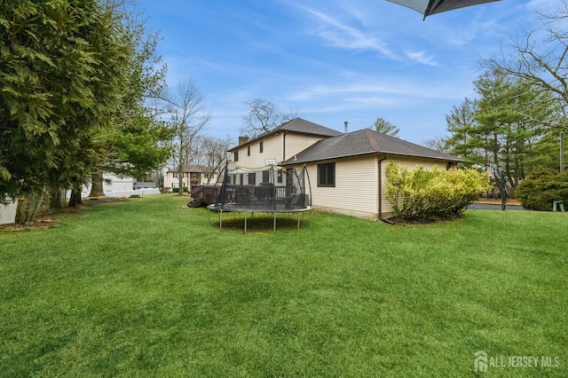 rear view of house featuring roof with shingles, a trampoline, a chimney, and a yard