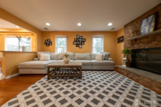 living room featuring a large fireplace, visible vents, baseboards, wood finished floors, and recessed lighting