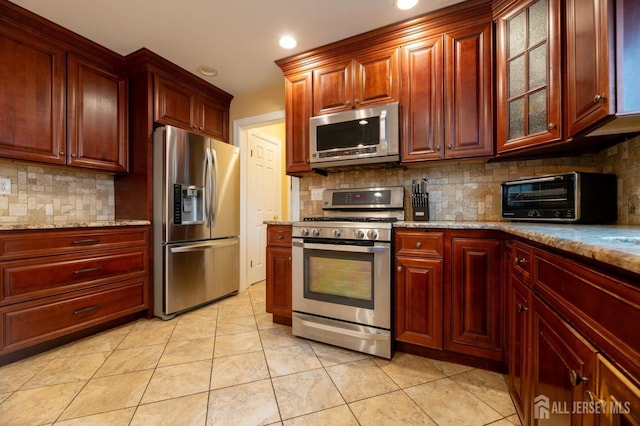 kitchen featuring stainless steel appliances, backsplash, light stone countertops, and a toaster