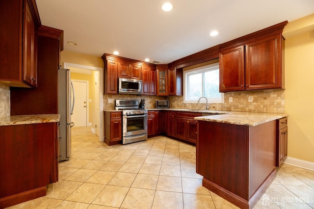 kitchen with light stone counters, stainless steel appliances, a peninsula, dark brown cabinets, and backsplash