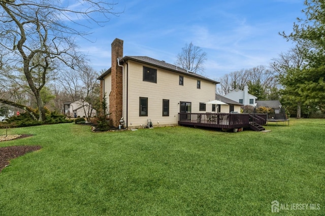 rear view of property with a trampoline, a chimney, a lawn, and a wooden deck