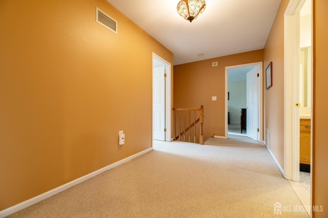 hall featuring baseboards, visible vents, light carpet, and an upstairs landing