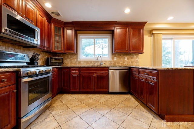 kitchen featuring stainless steel appliances, visible vents, dark brown cabinets, light stone countertops, and tasteful backsplash