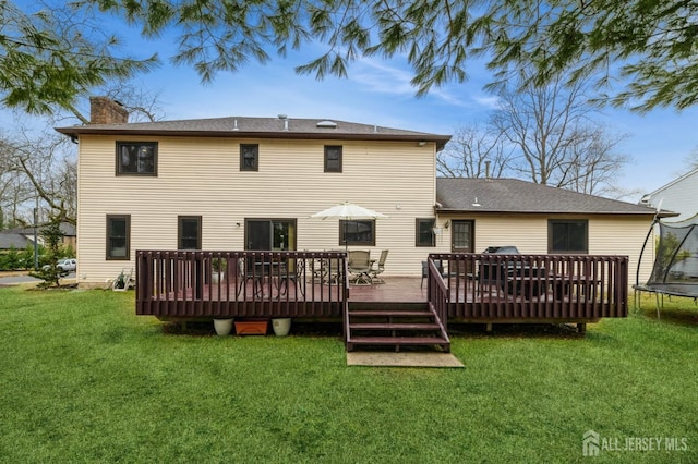 rear view of house featuring a trampoline, a chimney, a deck, and a lawn